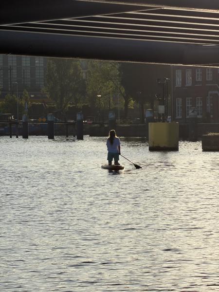 A lone figure is seen stand-up paddleboarding on the calm waters of the Rapenburg canal in Amsterdam, passing under the Mr